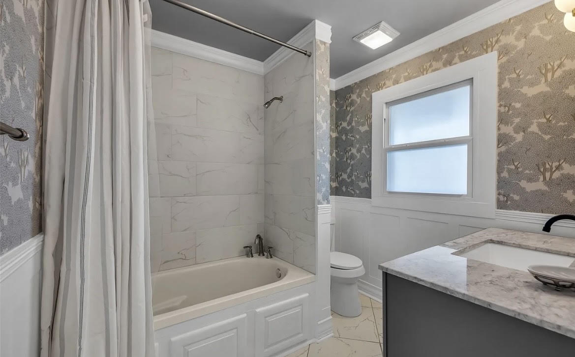 Updated bathroom with tiled tub surround, wallpaper, and stone vanity top